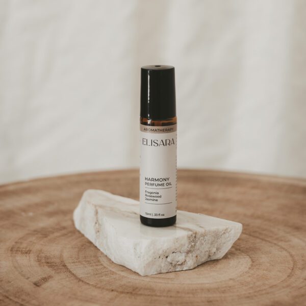 Amber 10ml roller bottle on a shard of white quartz on a timber table. Bottle is a calm essential oil blend of Australian Fragonia, lavender, rosewood, jasmine and grapefruit.