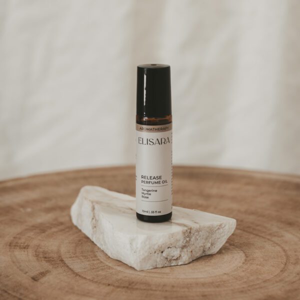 Essential Oil Roll On Perfume for Emotional Well-being with tangerine, myrtle, neroli and sandalwood in a 10ml amber bottle with white label sitting on a white quartz flat rock on a timber round with a white curtain behind.