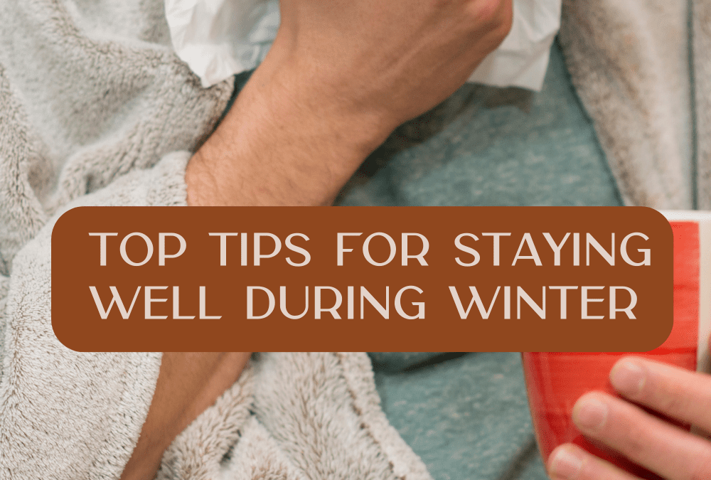 Image of a man in a white dressing gown sitting down using a tissue or hankie on his nose due to a cold. He is holding a red cup of tea and the caption over the top says "Top tips for staying well during winter".